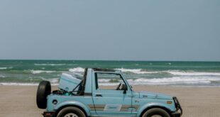 A classic blue SUV parked on the sandy Playa Chachalacas beach in Mexico under a clear sky.