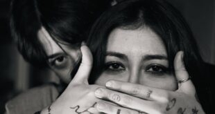 A dramatic black and white portrait featuring two adults with expressive hand tattoos.