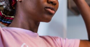 A woman adjusts her vibrant headscarf, promoting a blend of fashion and culture.