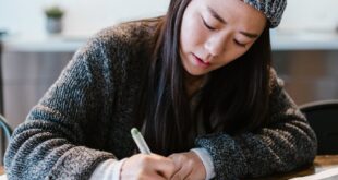 Focused young entrepreneur writing business notes in a cozy indoor setting wearing a warm beanie.