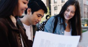 Group of young students reviewing documents outside a university building.