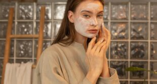 Woman applying a facial mask in a spa-like indoor setting for skincare and wellness.