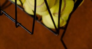Detailed view of tennis balls stored in a metal basket placed on a court.