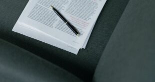 A pen resting on a stack of documents on a dark green sofa.