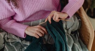 A woman knitting a handmade blanket with green yarn indoors, showcasing cozy and creative winter leisure.