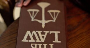 A close-up of a hand holding a law book on a wooden table, emphasizing legal studies.