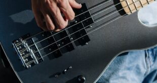 Musician performing with a sleek electric bass guitar in a home studio setting.