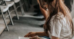 Focused woman reading a book in an academic setting with others in the background.