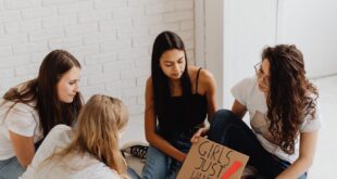 Group of women creating protest signs with art materials in a bright indoor space.