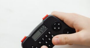 Close-up of hands using a compact black calculator on a white marble surface, displaying numbers.
