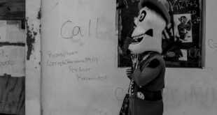 A person in a costume walks by a grafitti-covered wall in a black and white street setting.