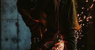 Worker in silhouette cutting metal with sparks in a construction site at sunset.