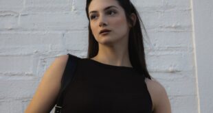 Elegant female model poses in front of a white brick wall during daytime, showcasing modern fashion.