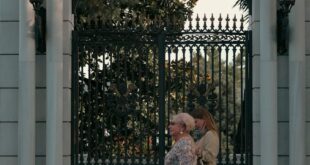 Two elegantly dressed women walk past the ornate gate of Galatasaray University in Istanbul, Turkey.