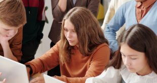 Group of teenagers in a classroom collaboratively working on laptops, fostering team learning.