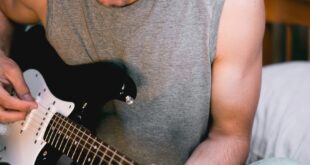Casual young man in stylish attire playing an electric guitar indoors, showcasing creativity and relaxation.