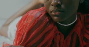 A woman lying on a bed indoors in Ghana, wearing a red shirt with a calm expression.
