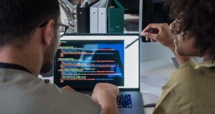 Two developers engage in software programming on a laptop in a modern office setting.
