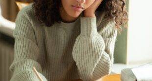 Teenage girl with curly hair studying at a desk, concentrated on her homework.