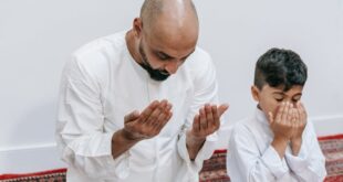 A father and son kneel in prayer together indoors, highlighting family and religious devotion.