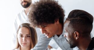 Group of professionals engaging in a collaborative discussion around a laptop in a modern office setting.
