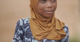 A young girl in a hijab smiles warmly, captured outdoors in Ghana.