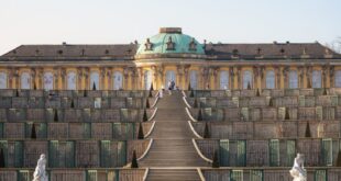 A breathtaking view of Sanssouci Palace's grand staircase and fountain under a clear blue sky.