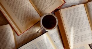 Top view of scattered open books with a cup of coffee in the center.