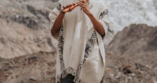 A man in traditional attire plays a flute in the scenic mountains of Peru.