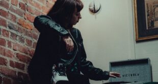 A moody indoor portrait featuring a woman with a vintage vinyl player and exposed brick wall.