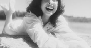 A cheerful adult woman with a big smile reclining on a rock by a serene lake, capturing a moment of pure happiness.