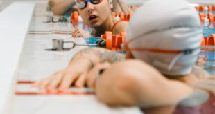 Swimmers in goggles and caps converse at an indoor swimming pool, capturing a dynamic athletic moment.