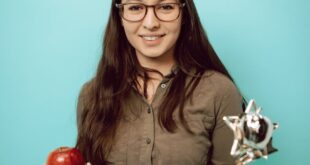 Smiling young woman in glasses holds an apple and a trophy on a blue background.