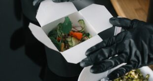 Gloved hands preparing fresh salad takeout in eco-friendly containers for delivery.