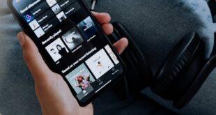 Close-up of a person holding a smartphone with headphones, browsing a music app.