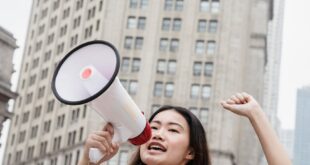 Young woman passionately speaking in protest with a megaphone in a city setting.