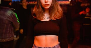 A woman stands in a stylish nightclub with vibrant neon lights and a lively atmosphere.