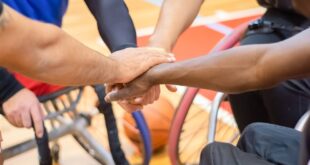 A diverse group of wheelchair basketball players united in a huddle indoors, emphasizing teamwork.