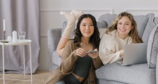 Two friends relaxing at home using a laptop and smartphone, showcasing comfort and connectivity indoors.