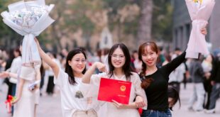 Three young women celebrating graduation with flowers and certificate outdoors.