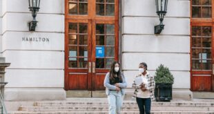 Multiracial women in casual clothes and masks carrying notebooks while going out from university