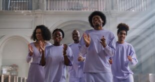 Joyful group singing in a church with sunbeams illuminating stained glass window.