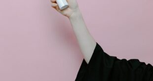 Hand of a graduate wearing a gown holding a diploma with a pink background.