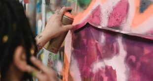 An artist skillfully applies vibrant spray paint to a graffiti mural in an urban setting.