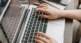 From above of unrecognizable woman sitting at table and typing on keyboard of computer during remote work in modern workspace