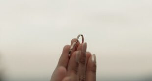 Close-up of hands exchanging engagement ring with blurred outdoor background.
