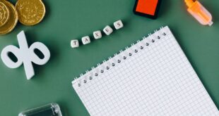 Flat lay of tax-related items on green background including coins, notebook, and calc.
