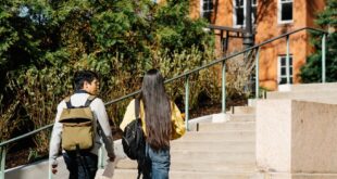 Two young adults walking up outdoor stairs surrounded by greenery and buildings.
