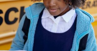 Curious child reading a textbook by a school bus, focusing on education and learning.