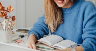 A cheerful woman in a blue sweater working remotely with a laptop in a cozy home setting.